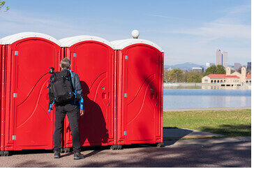 Red portable restrooms placed along a lakefront path with the city skyline in the background