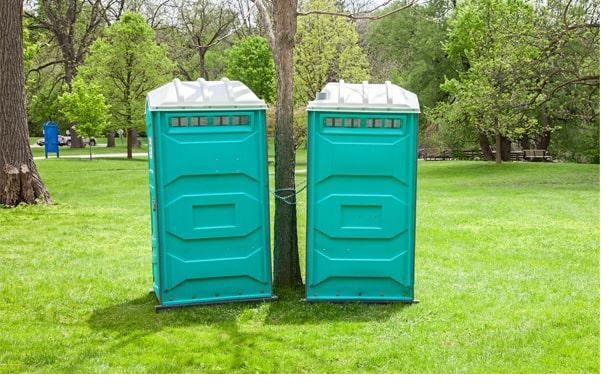 Two teal portable restroom units placed around a shade tree at a corporate event