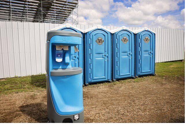 Portable hand-wash station standing beside a row of blue portable restrooms