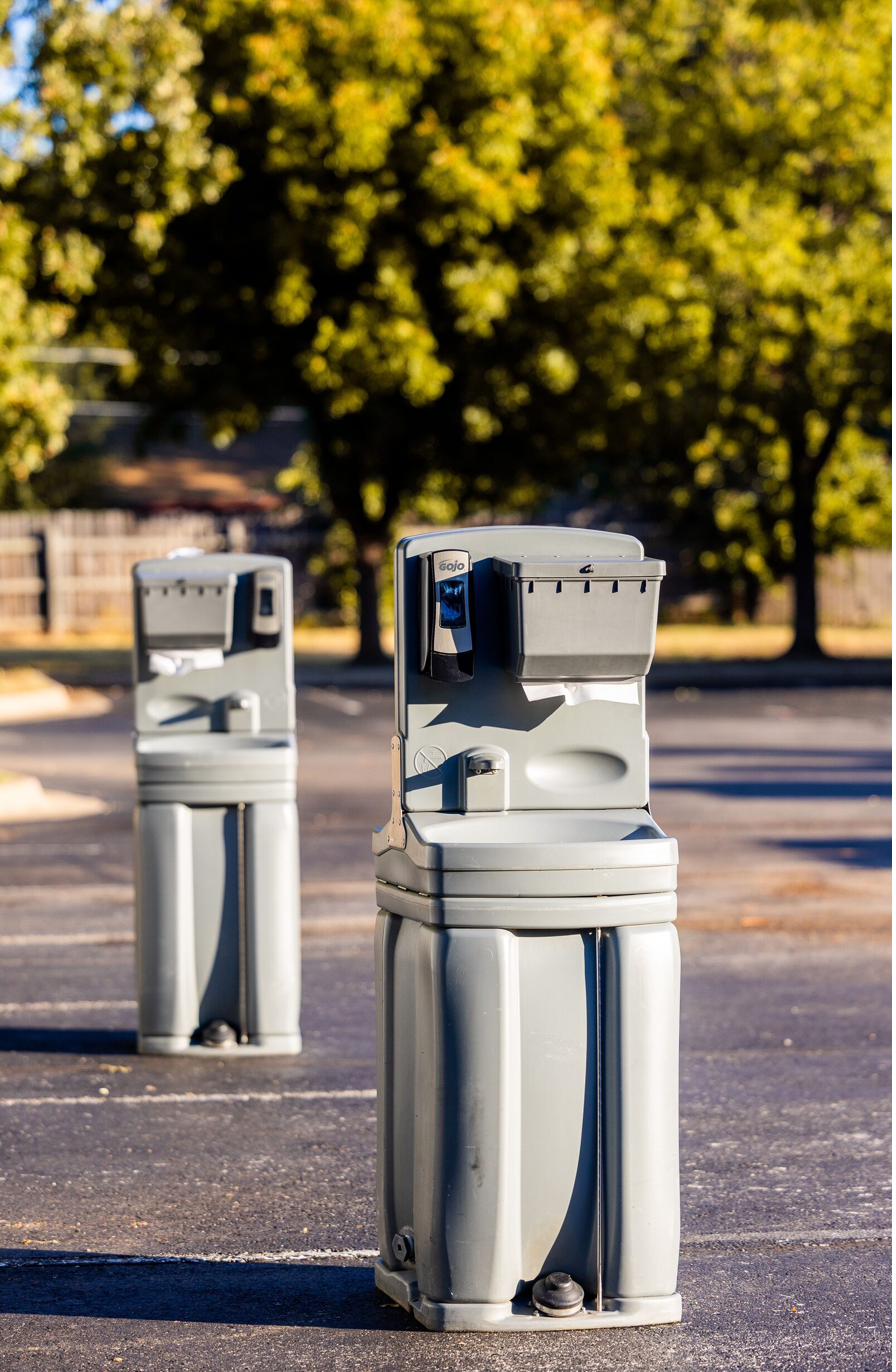 Two portable hand-washing stations set up in a parking lot